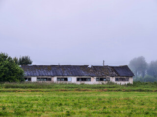 Obraz premium A large abandoned farm building with damaged windows and roof. High value of running agriculture business. Old worn out barn. Rising supply price and troubled economy effect on running a ranch.