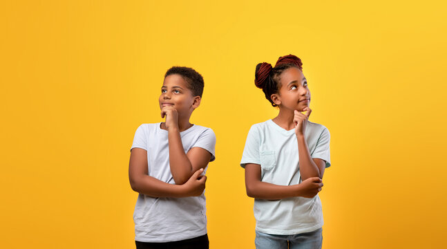 Pensive afro-american boy and girl posing on yellow studio background, black brother and sister thinking about something, touching chins and looking at copy space, panorama. Kids lifetime