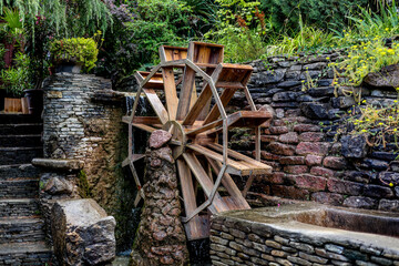 The photograph shows an old wooden mill that pumps water for watering the garden and vegetable garden. Beautiful green trees grow next to the wheel.