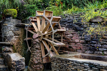 The photograph shows an old wooden mill that pumps water for watering the garden and vegetable garden. Beautiful green trees grow next to the wheel.