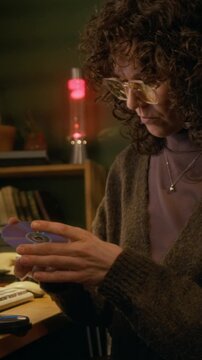 Medium vertical of busy Caucasian woman in glasses checking out stack of CD disks with software or files, putting back in box, while working on retro desktop computer at home