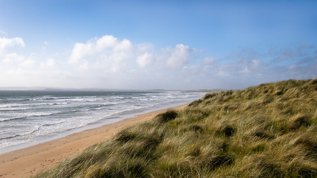 Waves crashing along the grassy shore and sandy beach of Laggan Bay on the Isle of Islay in Scotland.