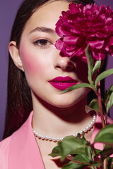 Young woman with bright pink lips and blush holding a big magenta flower near her face. Close-up...