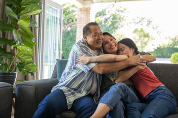 Naklejka premium Family embracing on gray sofa at home near open sliding glass door with potted plant