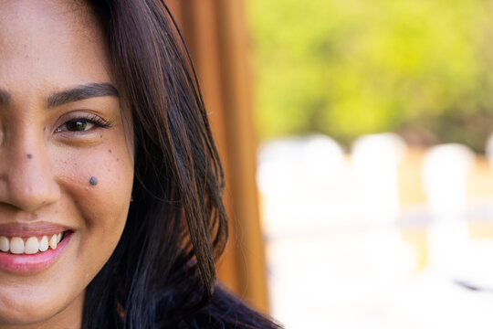 Mid-adult Asian woman smiling, wearing dark top and leaning near wooden post at sunlit patio