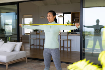 Mid-adult Asian woman holding yellow band stretching across chest on patio wearing pullover