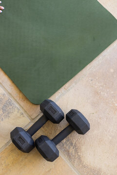 Pair of black hex dumbbells are resting on beige tiled floor near dark green mat