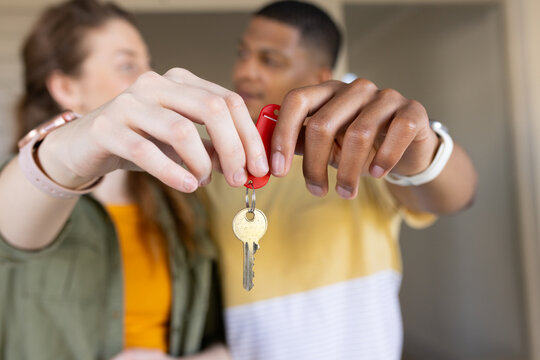 Diverse couple holding metal key with red fob in hall, green jacket, striped shirt showing watches
