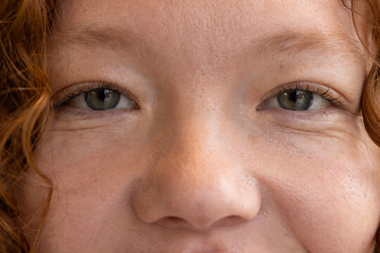 Teen female smiling softly, showing freckles and greenish-gray eyes inside room close-up