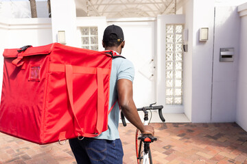 Red insulated delivery bag is dominating frame while bicycle is being pushed at house entrance