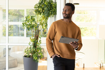 African American man in sweater standing in office holding tablet near glass partition, copy space