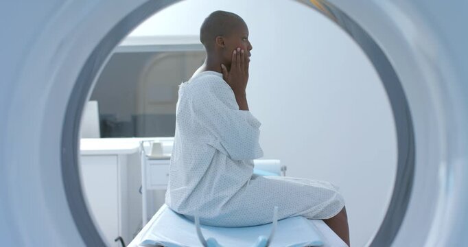 Adult African woman wearing hospital gown adjusting hands and preparing for scan in scanner bore