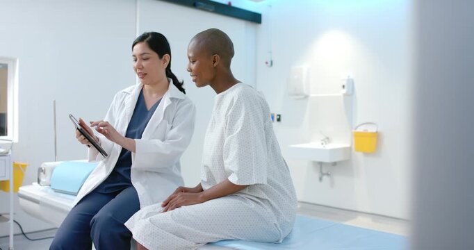Asian doctor in lab coat tapping tablet, showing care to African American patient on exam table