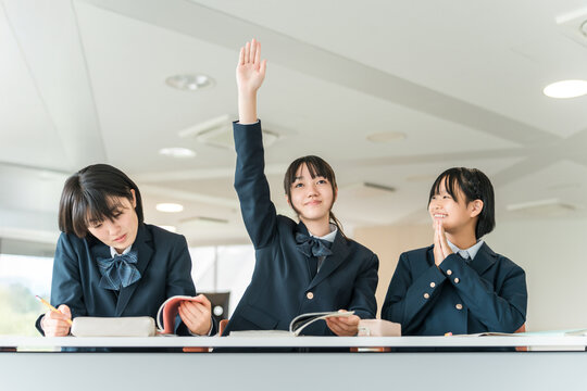 Active elementary school students, junior high school students, high school students, and female high school students (friends, classmates) in uniforms raising their hands during class in a school cla