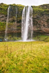 View of majestic Seljalandsfoss waterfall in Iceland, where powerful cascades of crystal-clear water plunge from towering cliffs into a misty pool below.