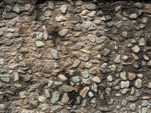 Seamless texture of a rustic wall made of small natural river stones, pebbles, and gravel embedded in concrete.