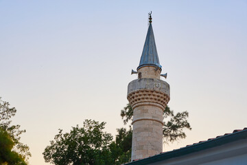 Fototapeta premium Historic stone minaret at sunset with clear sky and trees surrounding