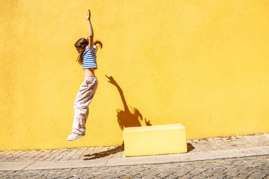 girl jumping off a block in front of a yellow wall