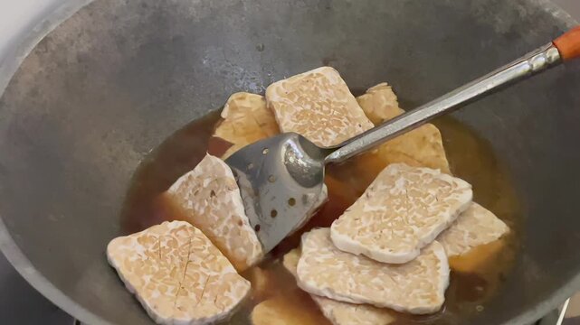 Preparing sliced raw tempeh in a traditional marinade sauce for cooking bacem
