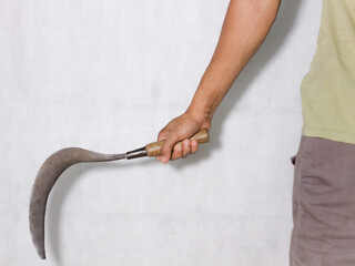 A hand holding a sharp curved knife or "Celurit" on a white background. A traditional farming tool from Indonesia.