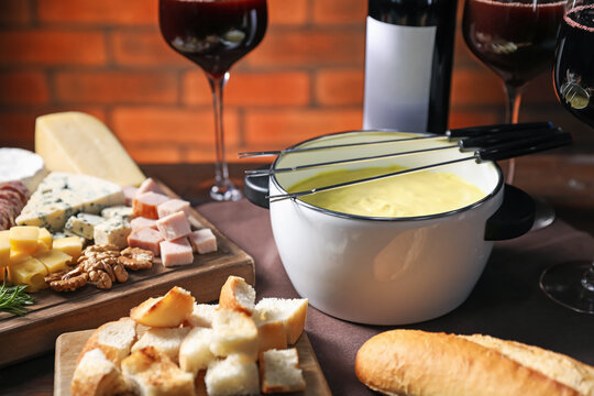 Fondue pot (caquelon) with melted cheese, wine and snacks on table, closeup