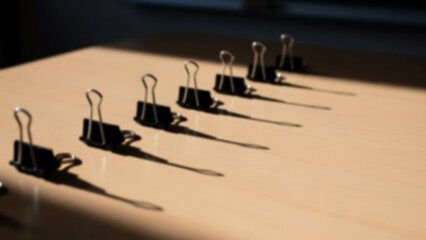 Obraz premium Blurred conceptual photo of binder clips aligned diagonally on a classroom table, strong light and shadow contrast