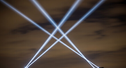 Bright spotlights shining upwards into the night sky during an outdoor event, creating an impressive display of light and energy.