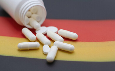 White medical capsules and tablets are scattered across the black, red, and gold stripes of the German flag.