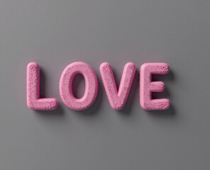 Pink, fuzzy three-dimensional letters spelling the word LOVE are prominently displayed against a uniform gray wall.