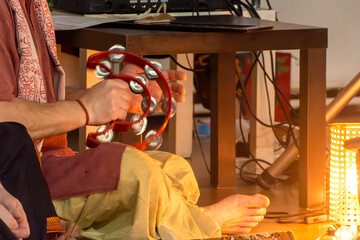 Close-up of hands gripping and shaking percussion instrument under warm ambient light. Traditional...