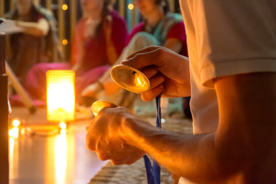 Close-up of hands striking traditional Indian percussion instrument under warm ambient light. Blurred background enhances focus on ritual action. selective focus