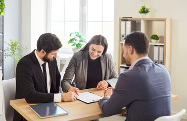 Businesspeople at desk, looking, signing contract documents, discussing content collaborating,...