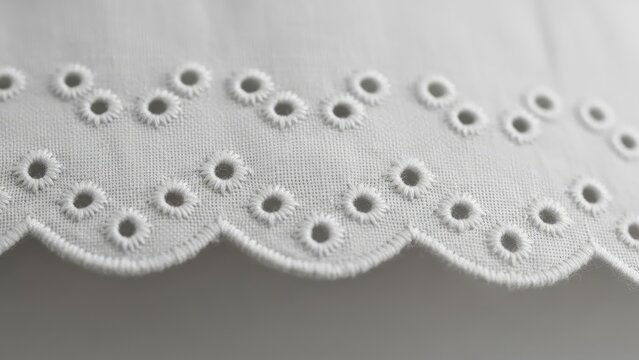 Close-up of white, embroidered fabric with eyelet holes and scalloped edge