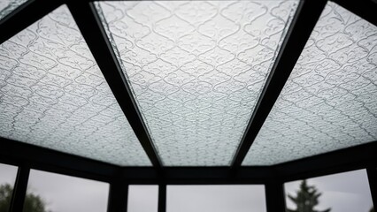 Glass roof panels with patterned design, supported by black framing, captured from below