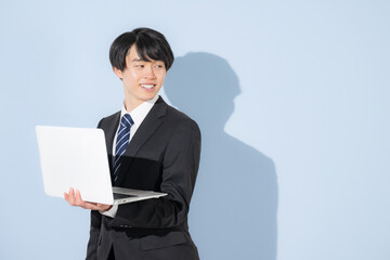 水色背景でパソコンを持つタイピングするスーツの若い大学生のような男性　新卒や就職のビジネスイメージ　就活の採用振り返る