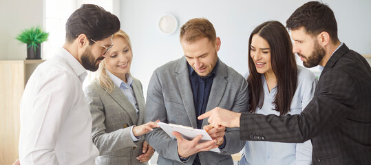 Group of five business professionals standing together in office and discussing document on...