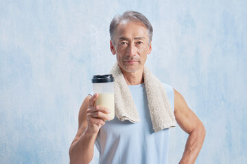 プロテインのボトルを持つトレーニングするシニア男性　カメラ目線