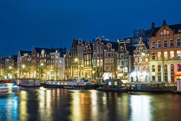 Obraz premium Discover the enchanting nights of Amsterdam, Netherlands, where historic buildings shine on the tranquil canals. A perfect scene for travel enthusiasts and showcasing the city s charm.