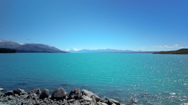 Sparkling Turquoise Lake With Rocky Shore And Distant Mountains
