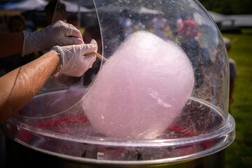 Hands spinning pink fairy floss at a country fair, giving a sense of whimsy and little kid...