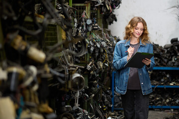 Woman carefully inspecting a junkyard with pen and clipboard