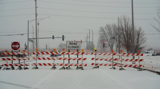 A wide view of intersection blocked by road closure barriers and warning signs during winter weather. traffic restrictions, public safety, caused by snow and road conditions.