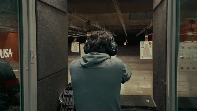 POV of person actively shooting a handgun at paper targets inside indoor shooting range. Controlled firearm use, marksmanship training, and safe target practice.