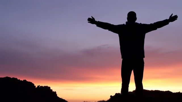 Silhouette of a person with outstretched arms against a vibrant, colorful sunset background