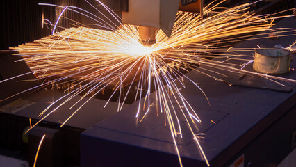 Cutting metal with a laser machine, the laser head cuts the metal, sparks fly when it comes into...