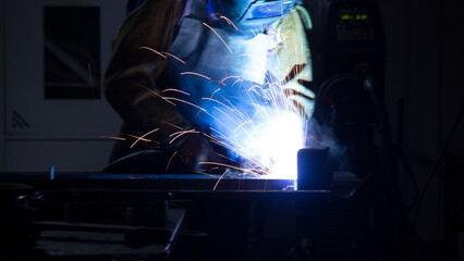 Manual metal welding, welding work in a mask, welding arc, sparks in the dark, bright flash of a welding arc, industrial welding in a protective suit, welding mask