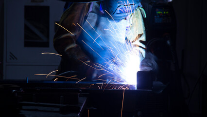Manual metal welding, welding work in a mask, welding arc, sparks in the dark, bright flash of a welding arc, industrial welding in a protective suit, welding mask