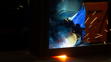 Manual metal welding, welding work in a mask, welding arc, sparks in the dark, bright flash of a welding arc, industrial welding in a protective suit, welding mask