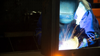 Manual metal welding, welding work in a mask, welding arc, sparks in the dark, bright flash of a welding arc, industrial welding in a protective suit, welding mask