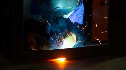 Manual metal welding, welding work in a mask, welding arc, sparks in the dark, bright flash of a welding arc, industrial welding in a protective suit, welding mask